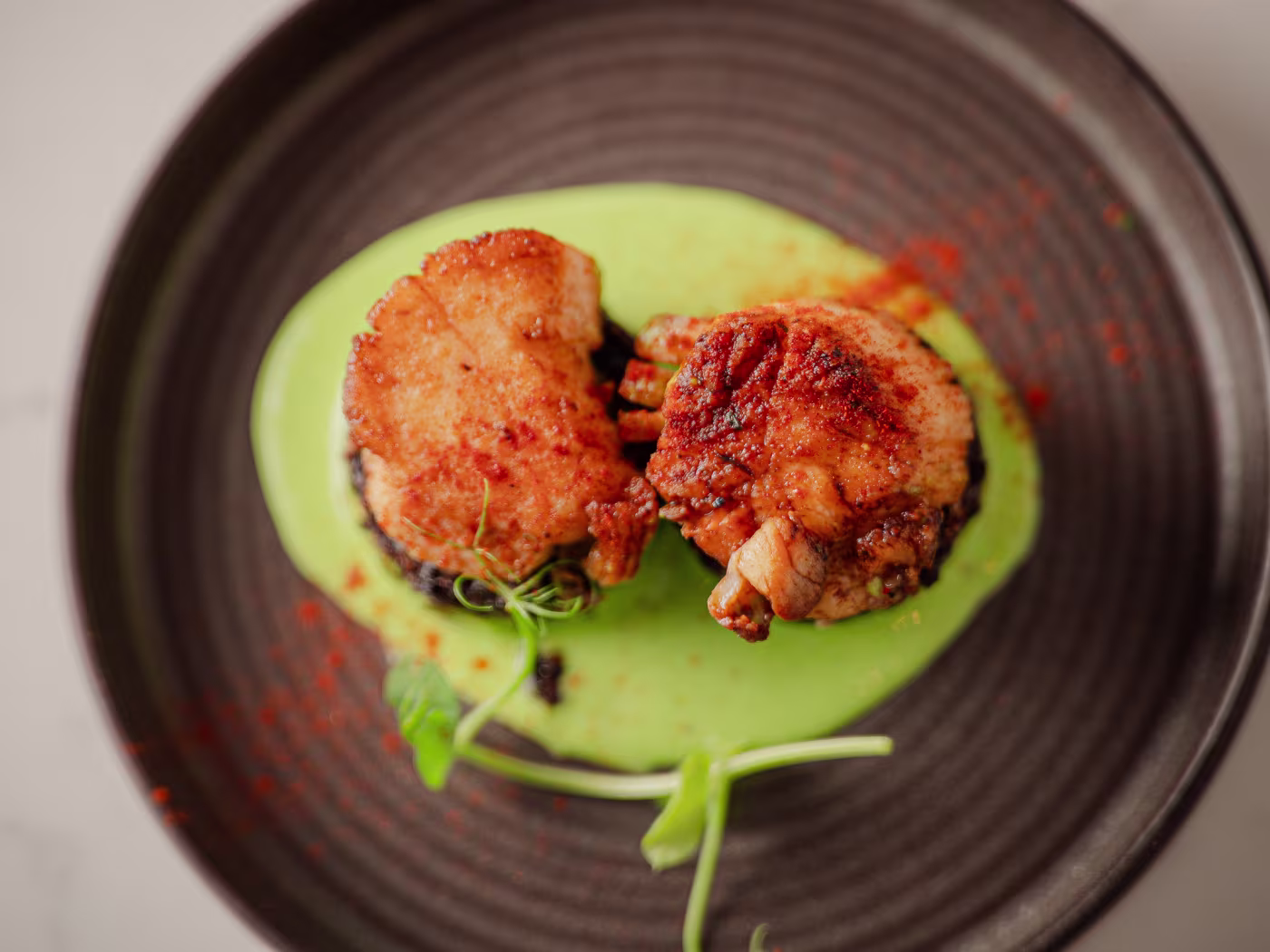 Croquetas caseras sobre crema verde en plato oscuro